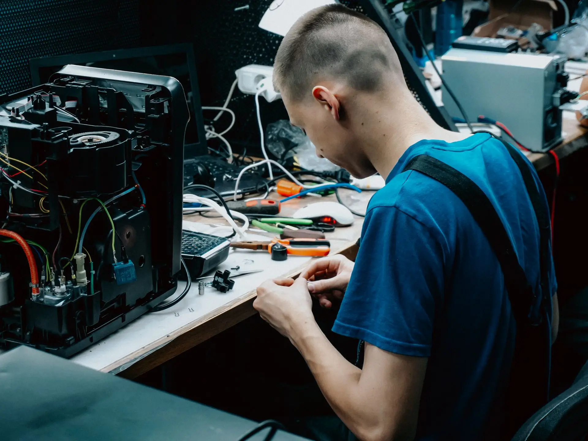 Tecnico al banco di laboratorio che ripara un apparecchio elettronico aperto, circondato da attrezzi